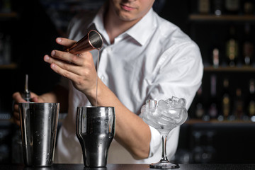 Bartender mixologist is pouring sugar syrup from a jigger into shaker.