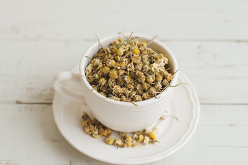 Dried chamomile flowers in a white tea cup on wooden table. Herbal tea
