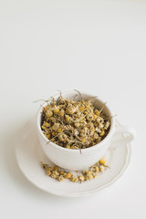 Dried chamomile flowers in a white cup. Herbal tea, vertical photo