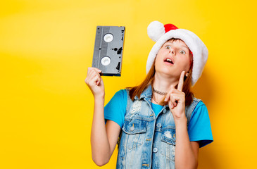 portrait of young teenage girl in Christmas hat with VHS on yellow background