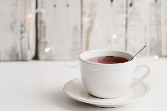 Red tea in a small white cup on white table, wood and small yellow lights as background