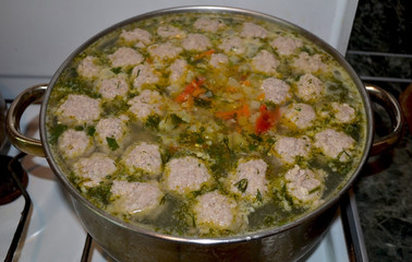 Vegetable soup with meatballs is cooked in a saucepan on the stove