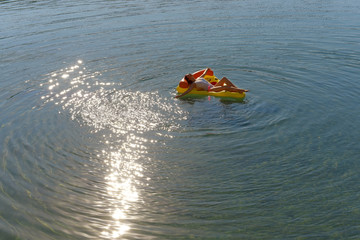 A beautiful young woman relaxes on an inflatable  sun bed in the middle of a lake. She wears a...