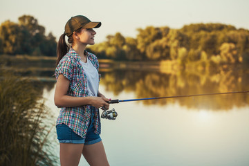 La femme mignonne pêche avec la canne sur le lac