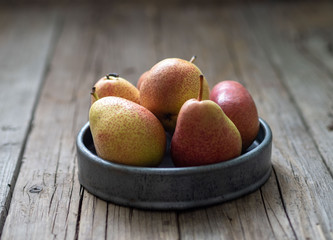 red-green pear cultivar forelle in gray bowl on wooden table, side view