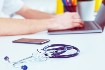 Stethoscope with smartphone and laptop on the desk. Male doctor working in hospital writing a prescription, Healthcare and medical concept. Selective focus