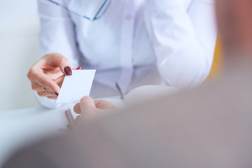 Female physician hand give white blank calling card to businesswoman closeup in office.