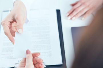 Female physician hand give white blank calling card to businesswoman closeup in office.
