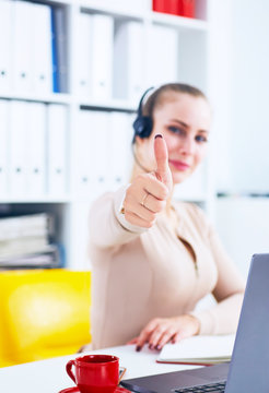Cheerful smiling female customer service operator showing thumbs up in office.