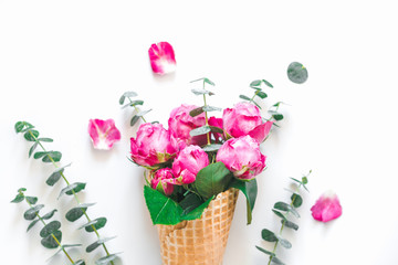 Still life of a bouquet of pink roses and eucalyptus inside a waffle cone on white background. The concept of gift and celebration. Flat lay, top view.