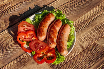Grilled sausages with fresh vegetables on wooden table