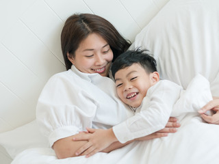 Beautiful asian mother and her little son playing and relaxing in bed at home. Happy mother's day. Lovely family concept.