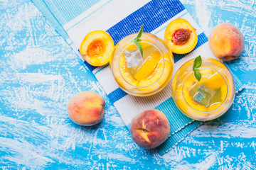 ripe peaches cocktail with ice and fresh mint on a blue table