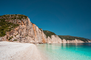 Fototapeta na wymiar Fteri beach in Kefalonia Island, Greece. One of the most beautiful untouched pebble beach with pure azure emerald sea water surrounded by high white rocky cliffs of Kefalonia