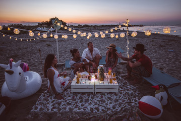 Group of friends making party on the beach at sunset time