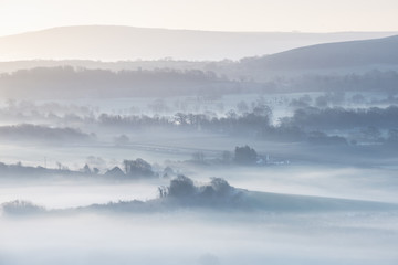 Stunning foggy English rural landscape at sunrise in Winter with layers rolling through the fields