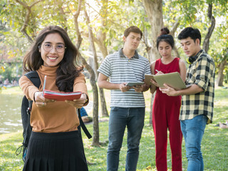 Beautiful asian college student holding books and smiling while his friends standing on background