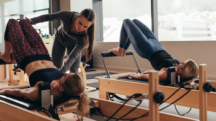 Female pilates trainer helping a pilates woman during training - obrazy, fototapety, plakaty
