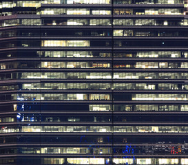 stacked floor office. night time light emmitted from modern curtain wall glass claded building in business area district. urban life style and electrical energy concumption concepts