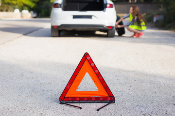 Triangular sign of the accident on the background of a girl about to change the wheel