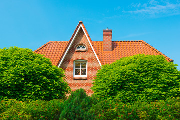 Fototapeta na wymiar Roof of the typical german house hidden in bushes. Clear blue sky on the background