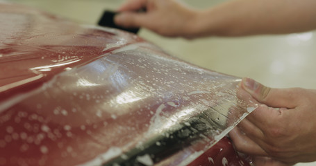 professional applying protective film to the red car