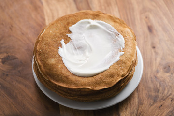 stack of fresh hot crepes or blinis with sour cream on wood table