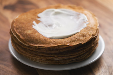 stack of fresh hot crepes or blinis with sour cream on wood table