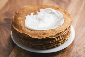 stack of fresh hot crepes or blinis with sour cream on wood table
