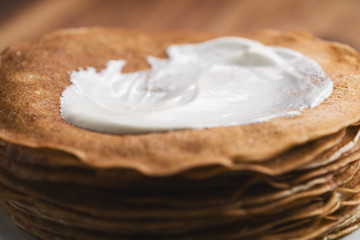 close-up of stack of fresh hot crepes or blinis with sour cream on wood table