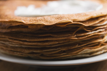 close-up of stack of fresh hot crepes or blinis with sour cream on wood table
