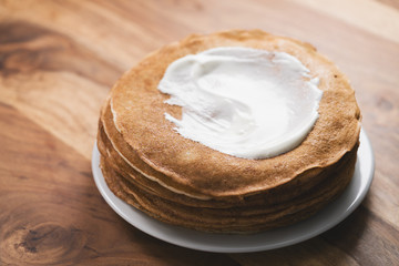 stack of fresh hot crepes or blinis with sour cream on wood table