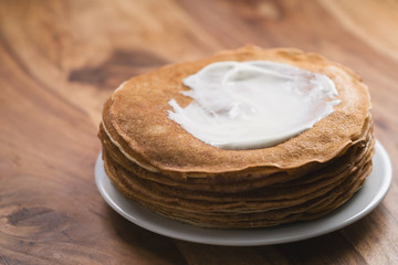 Fototapeta na wymiar stack of fresh hot crepes or blinis with sour cream on wood table