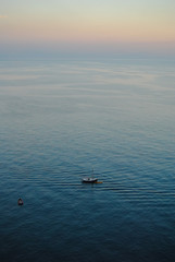 A small boat in the middle of the sea,  all alone in a peacefull and quiet sunset. Shot from above and gives aerial view of the sea and the sky