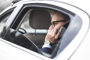 Naklejka premium young successful businessman talking on the phone sitting in the back seat of an elite car, talks and business meetings
