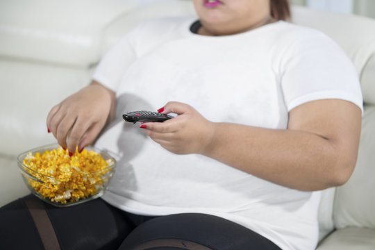 Closeup of overweight Asian woman with a bowl of popcorn watching TV
