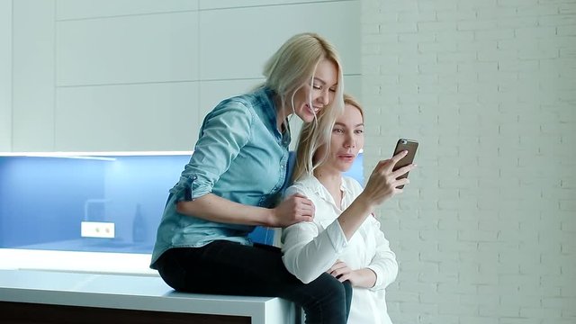 Two white women watching photos on the smartphone and laughing