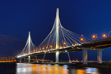 Obraz premium The bridge of circle highway road over Neva river near the mouth of it in the blue hour after the sunset. Night view on the buildings of Petersburg city and the Finish gulf
