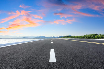 Asphalt road and lake with mountains at beautiful sunset