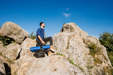 A traveler man with backpack and sunglasses sitting on the rocks at the mountais