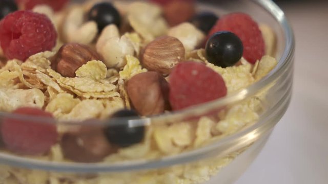 Rotating corn flakes with nuts and fresh berries in a glass bowl