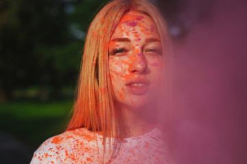 Fashionable caucasian young woman posing with exploding pink dry paint at Holi festival
