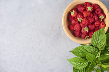 fresh and ripe raspberry in wooden bowl, green leaves