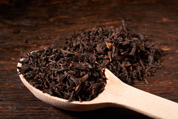 Leaves of black tea in wooden spoon on dark wooden table on black background