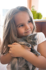 A little girl is very emotionally holding a kitten.