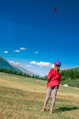 Obraz premium Little girl plays with her kite in large mountain meadows