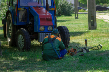Obraz premium Lazy worker rests after cutting the lawn. A city utility worker is sitting on the grass and talking on the phone. The worker idles during working hours near the tractor.