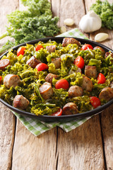 Warm salad of fried kale cabbage with sausages, tomatoes and garlic close-up on a plate. vertical