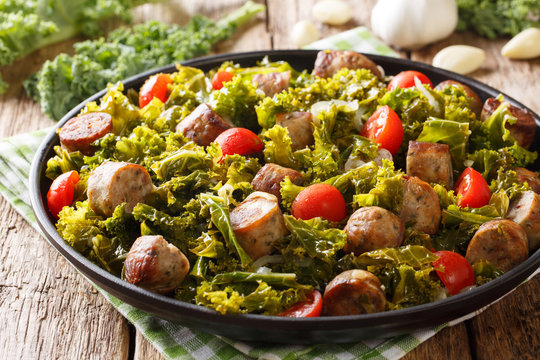 Stew kale leaf cabbage with sausages, tomatoes and garlic close-up on a plate on a table. horizontal