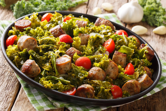 Spicy kale cabbage with fried sausages, tomatoes and garlic close-up on a plate. horizontal